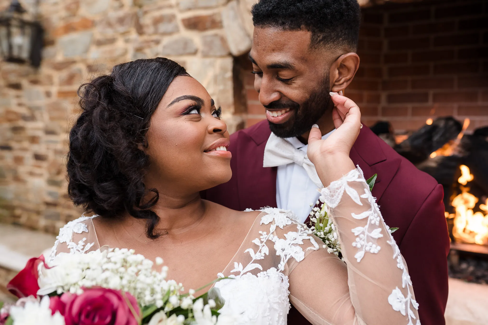 Bride touching her groom's face in front of an outdoor fireplace