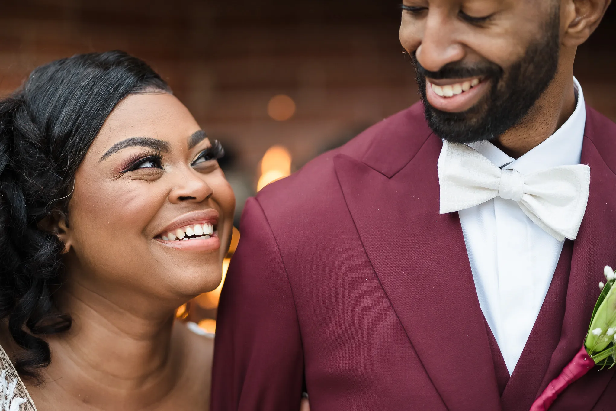 Bride smiling up at her groom in a burgundy suit and white bow tie