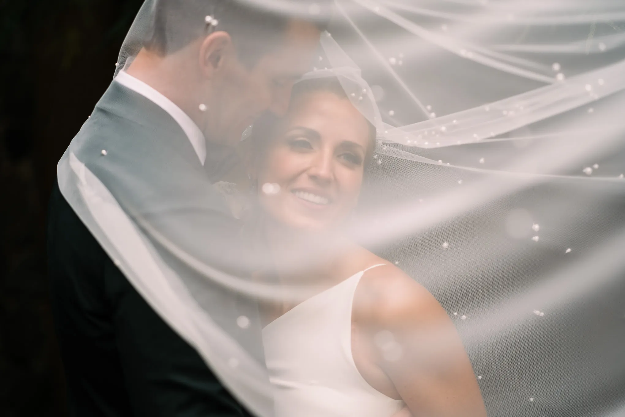 Groom holding his smiling bride under her veil