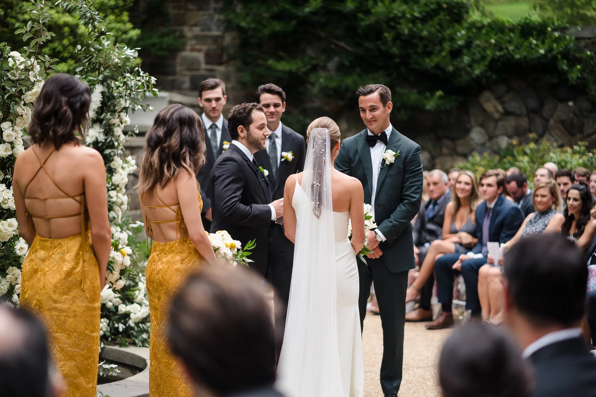 Bride and groom at the altar of an outdoor ceremony, bridesmaids in gold beside them
