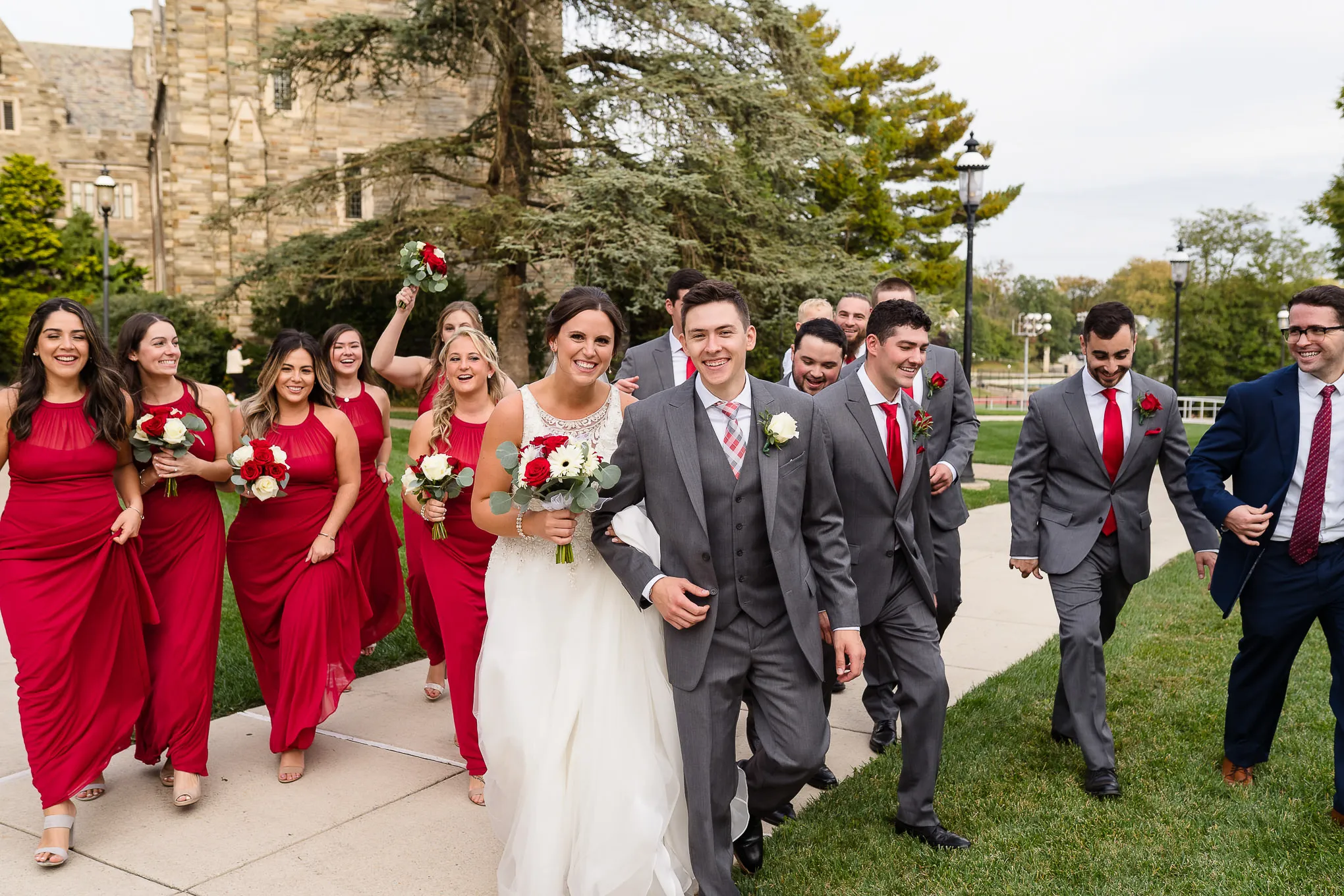 Bridal party walking together across a lawn, bridesmaids in red