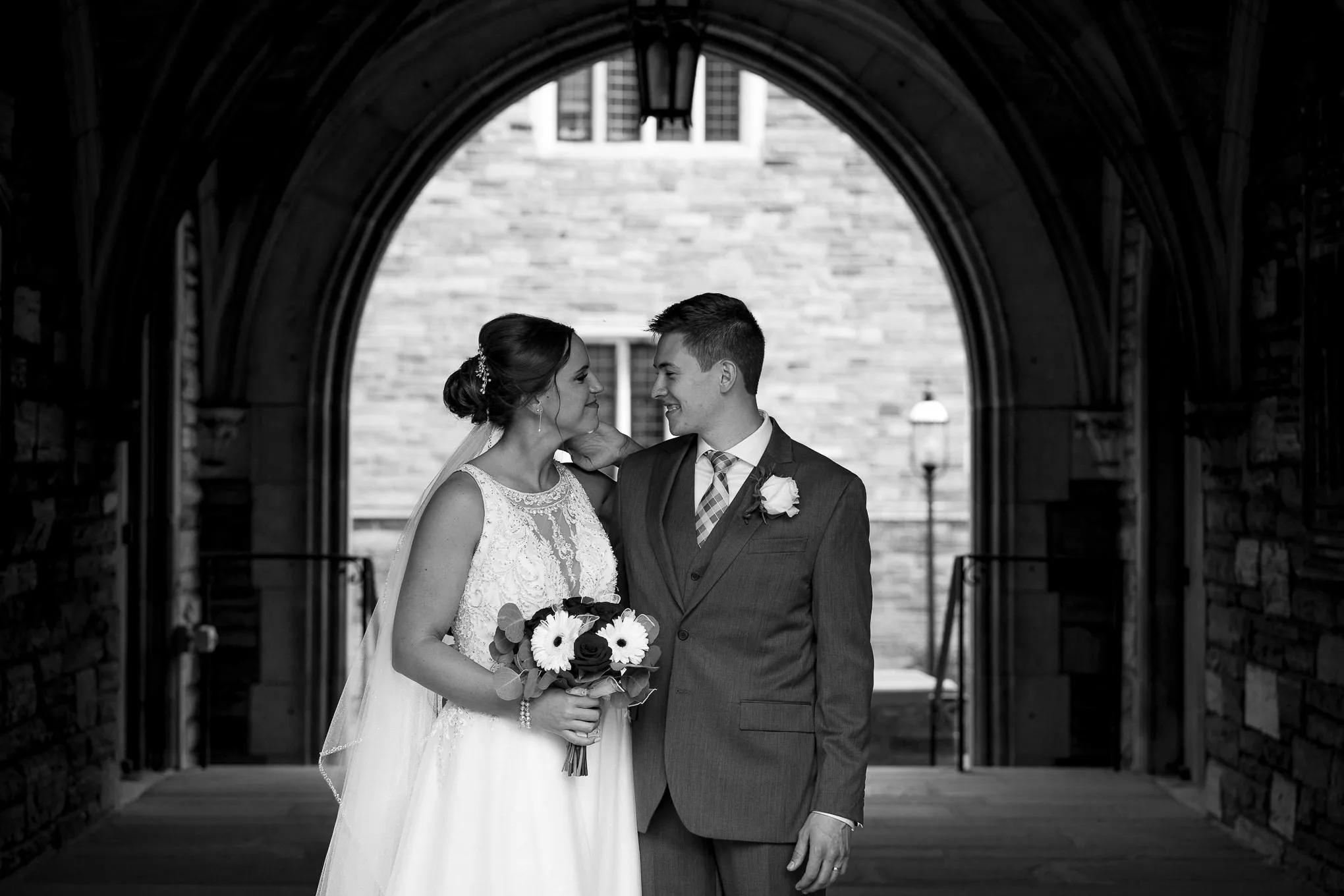 Black and white photo of a bride and groom under a stone archway