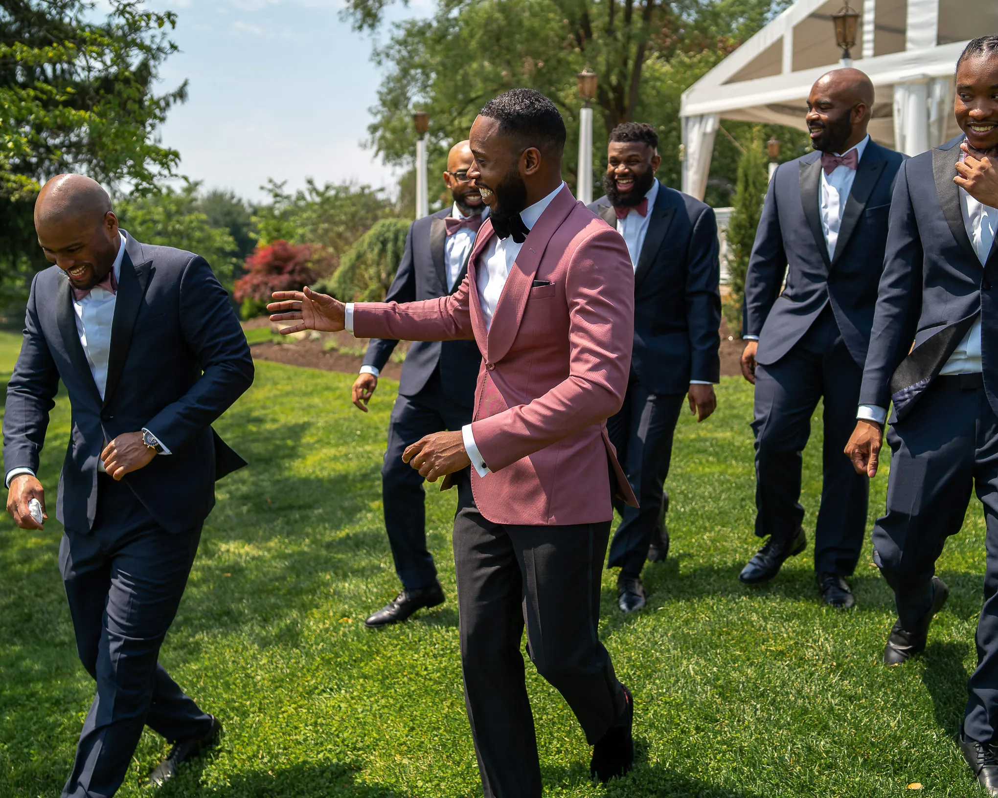 Groom in a pink jacket laughing with his groomsmen on a lawn