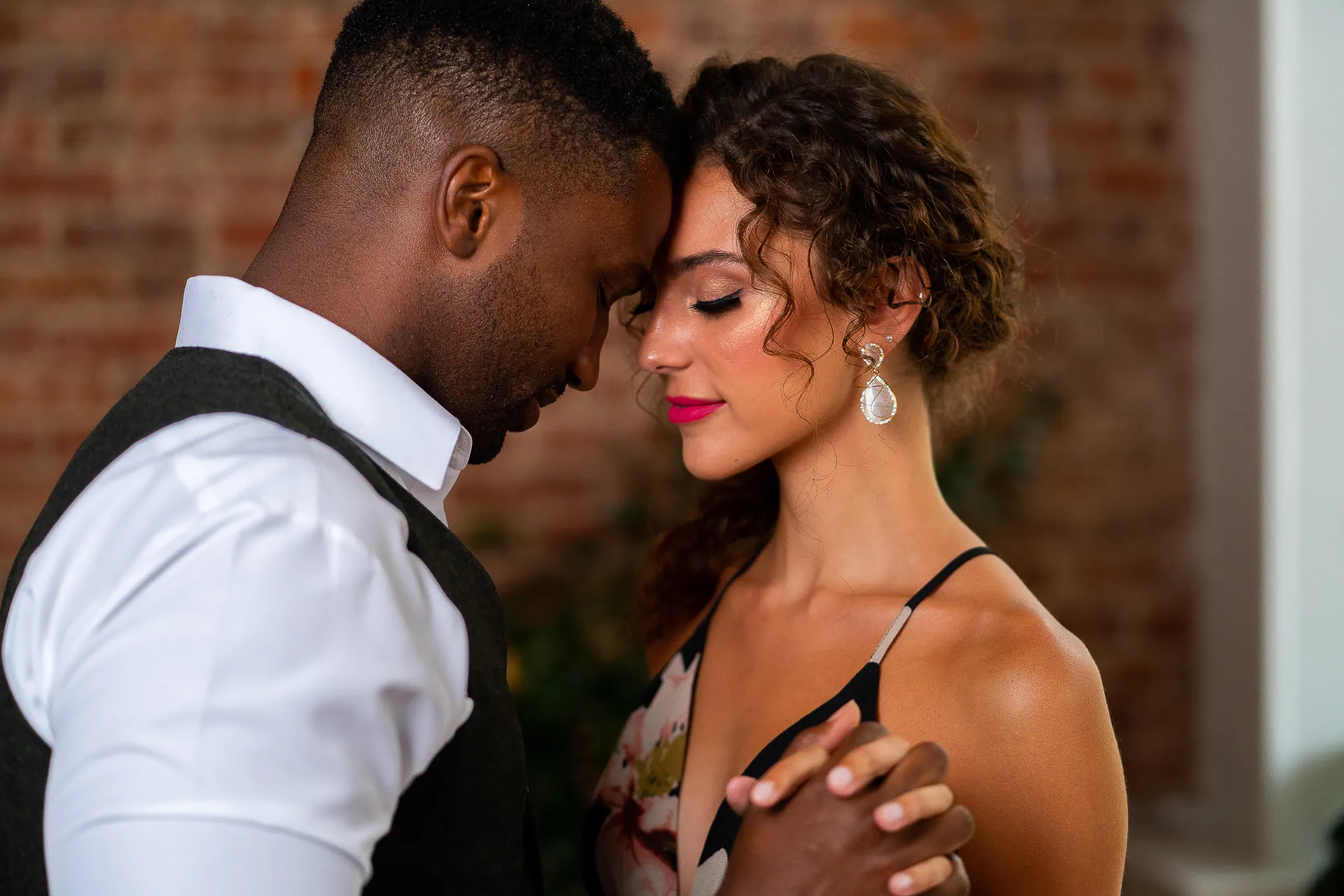 Couple touching foreheads against an exposed brick wall