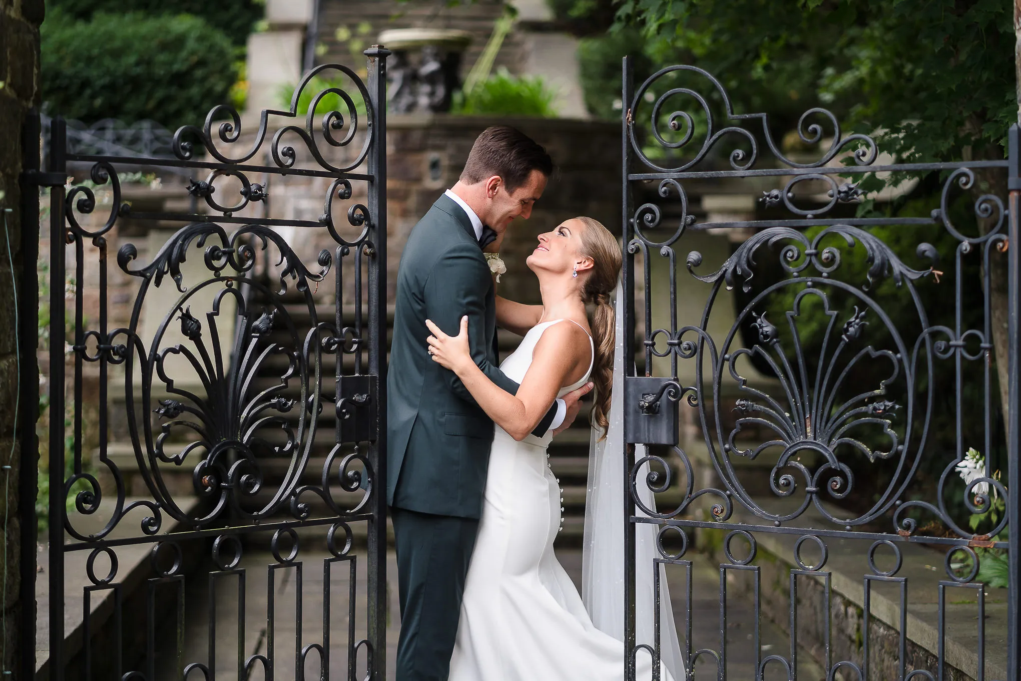 Groom and bride embracing between open wrought-iron garden gates
