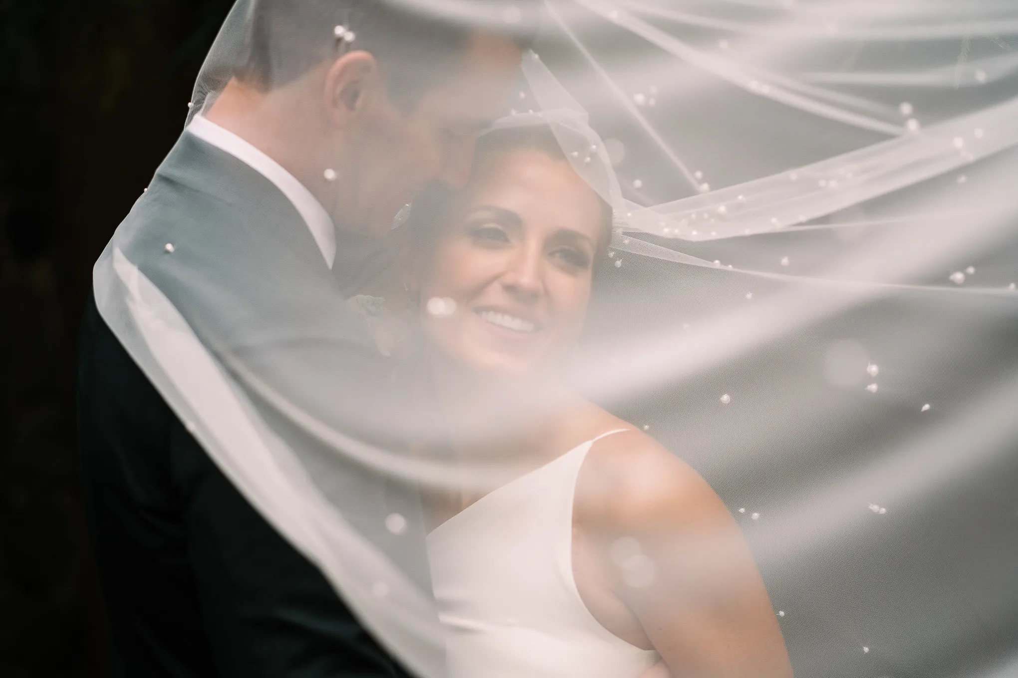 Groom holding his smiling bride under her veil