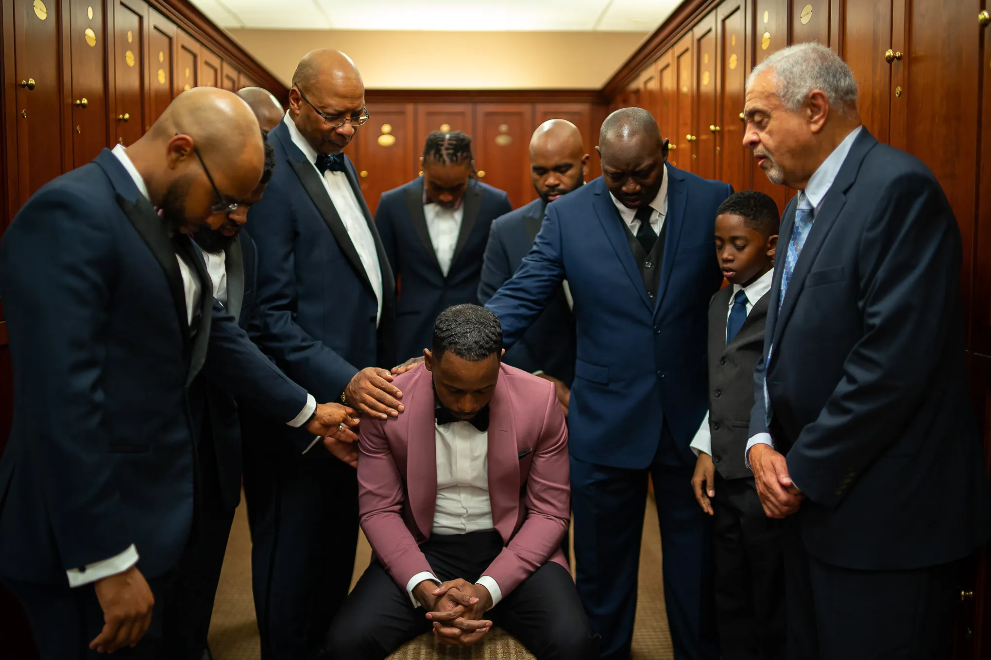 Groomsmen and family laying hands on the groom in prayer before the ceremony